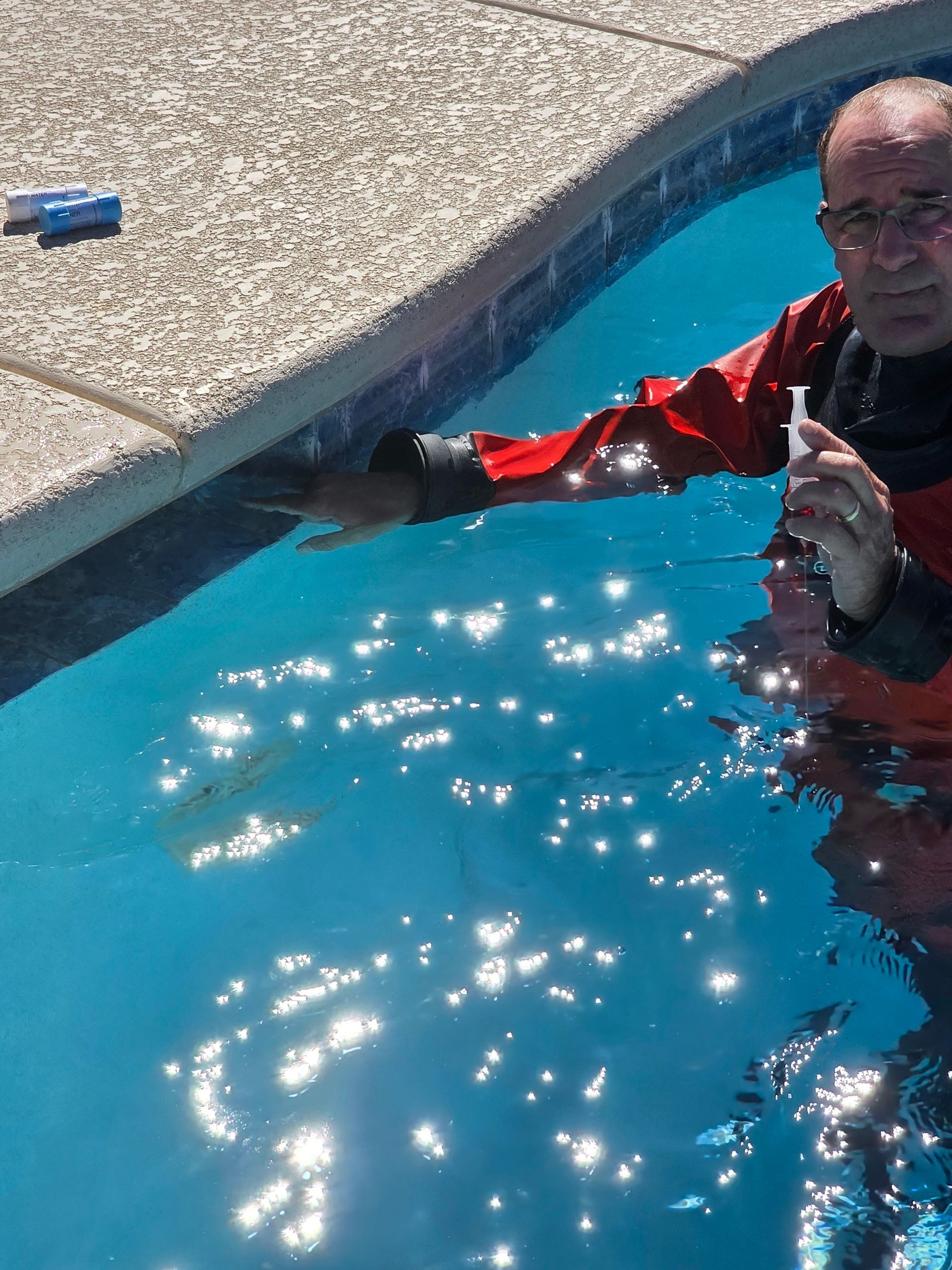 Person in a red jacket standing in a swimming pool, holding the pool edge and smiling.