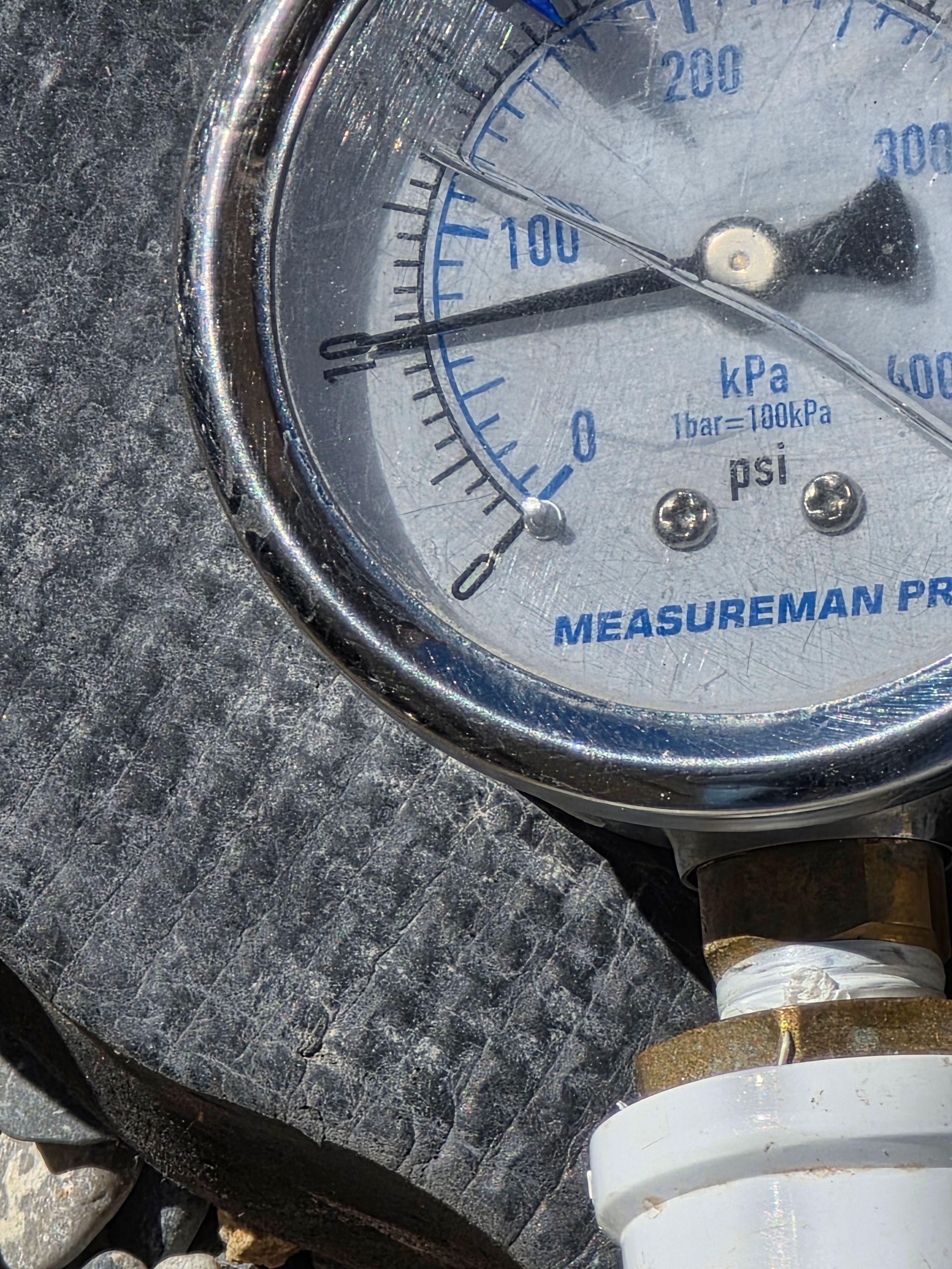 Close-up of a pressure gauge showing near 0 psi on a black hose fitting.