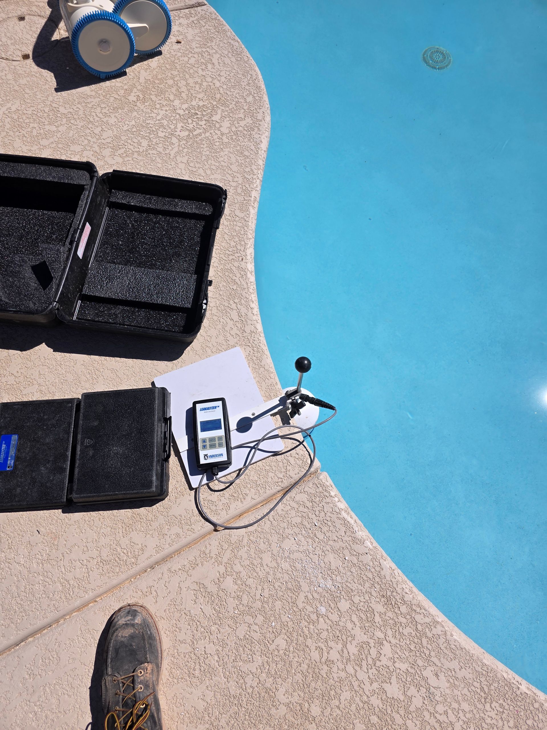 Poolside scene with cleaning gear, a rope, and a device beside the bright blue pool water.