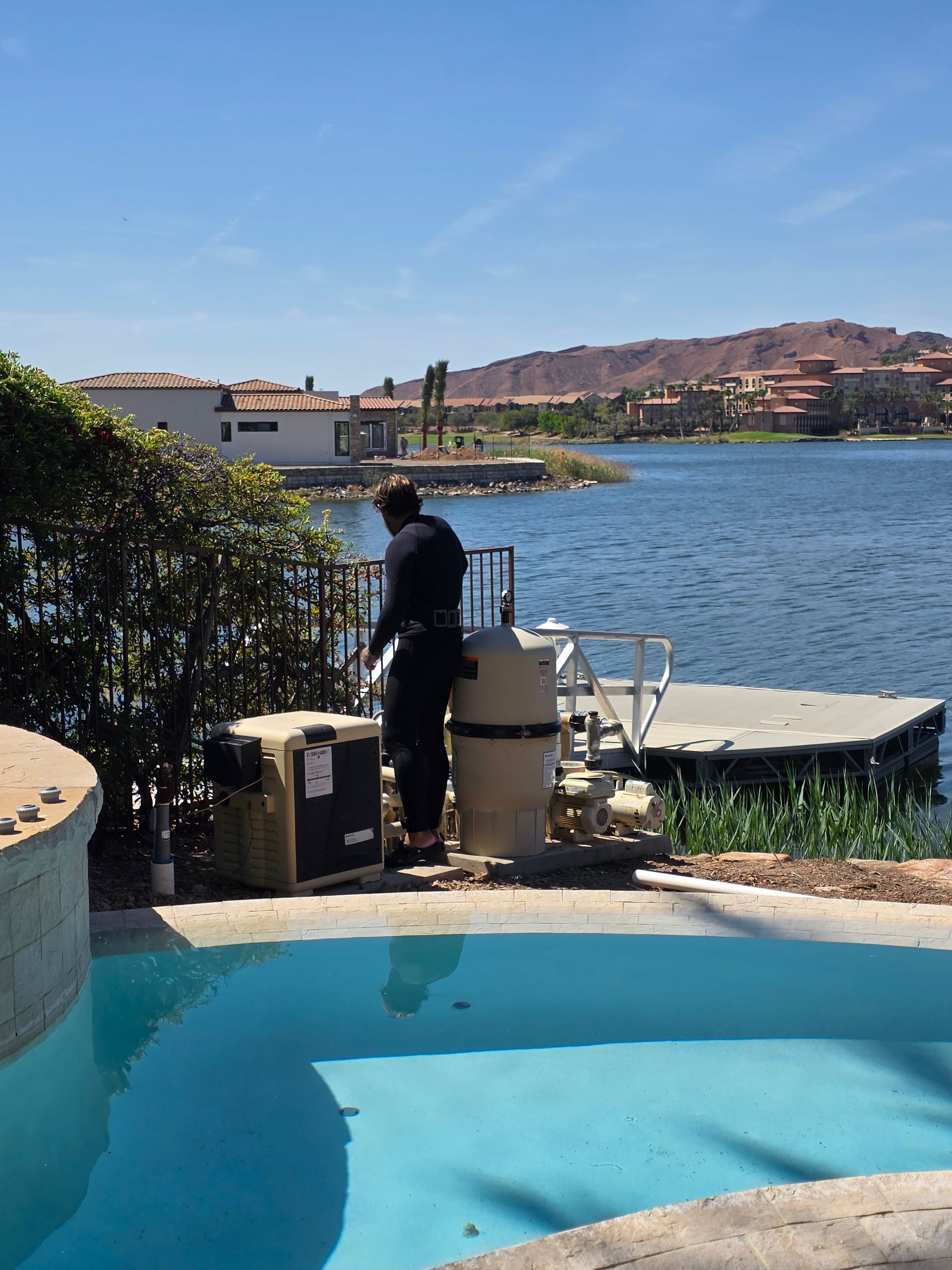 Person standing by a pool overlooking a waterfront bay and hillside homes