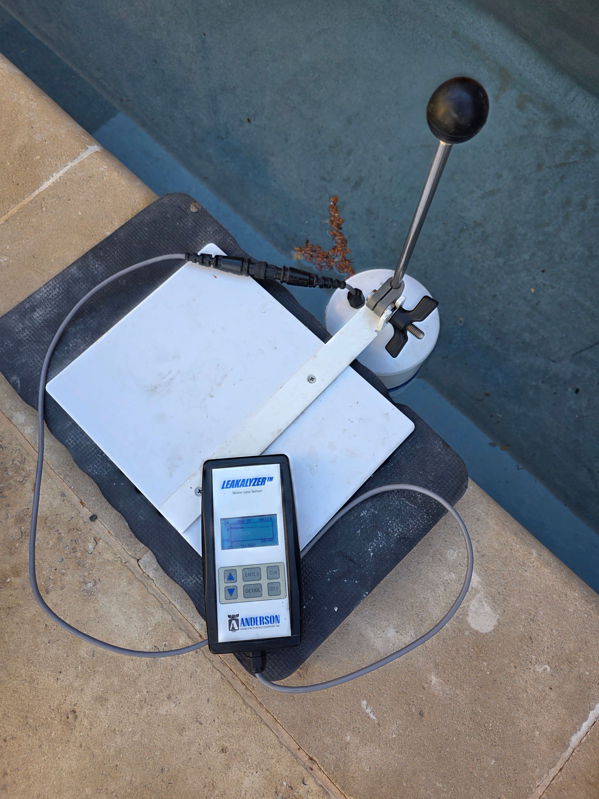 Handheld measuring device next to a metal lever on a white platform by a blue wall, with cables attached