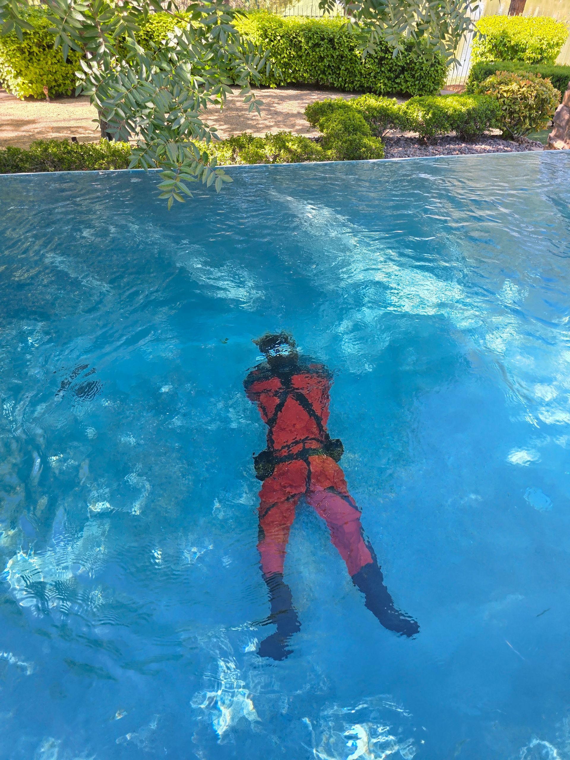 Person in a red suit floating face down in blue water near a leafy riverbank