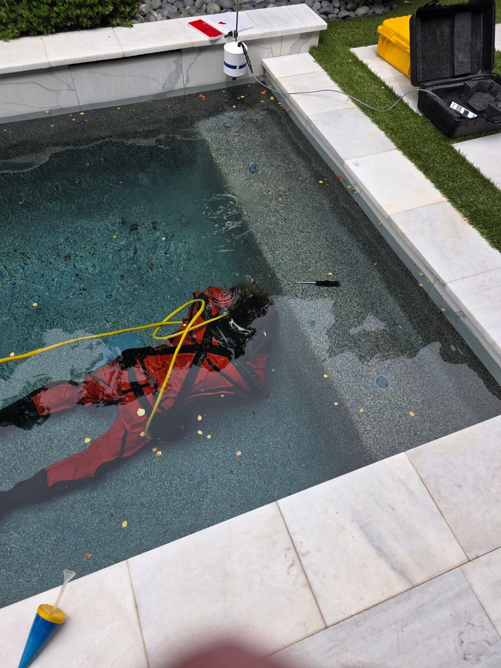 Person in red and black floating in a pool beside a fountain and tiled patio