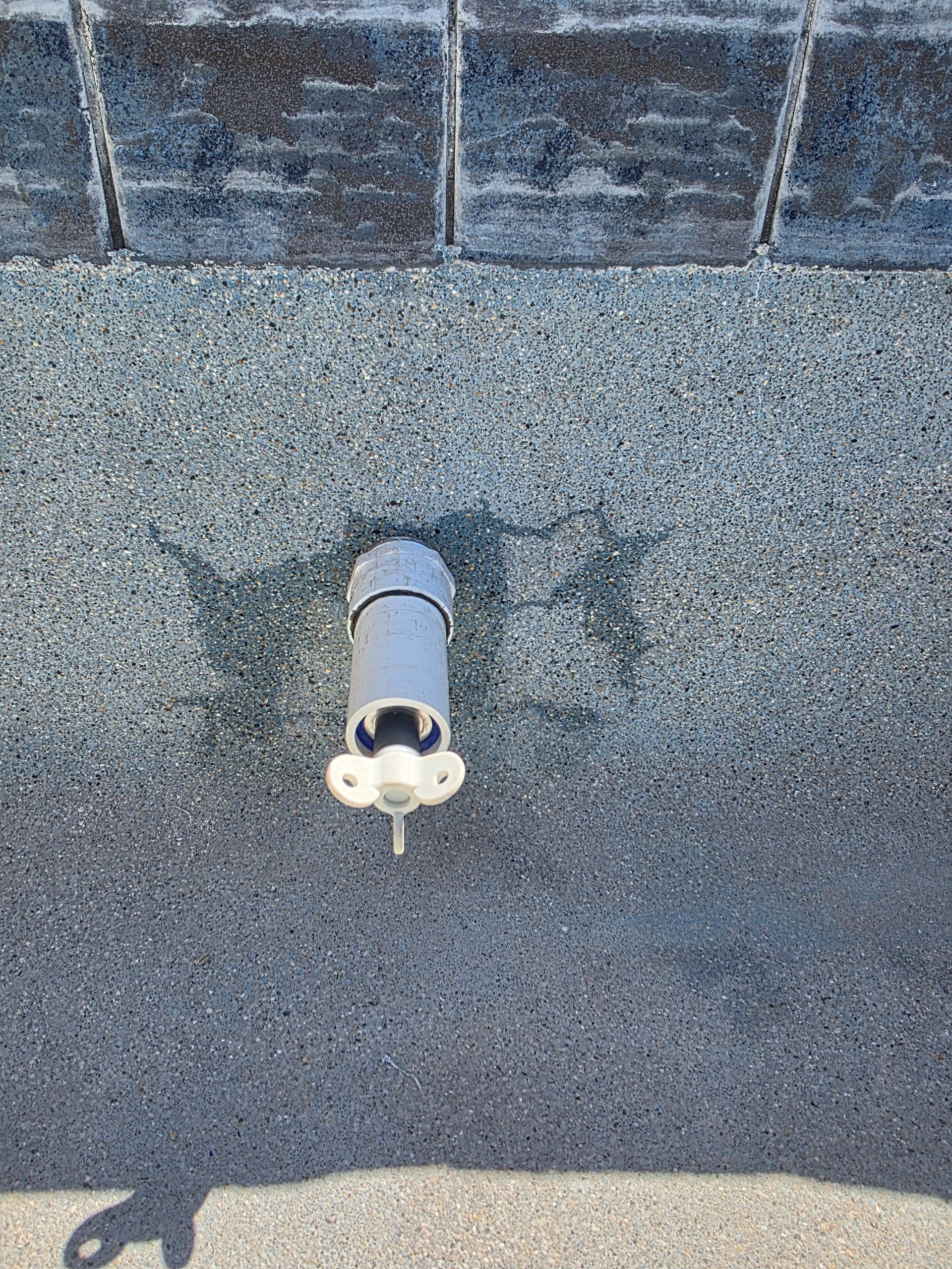 Small white pipe fixture protruding from a gray wall under blue tile siding