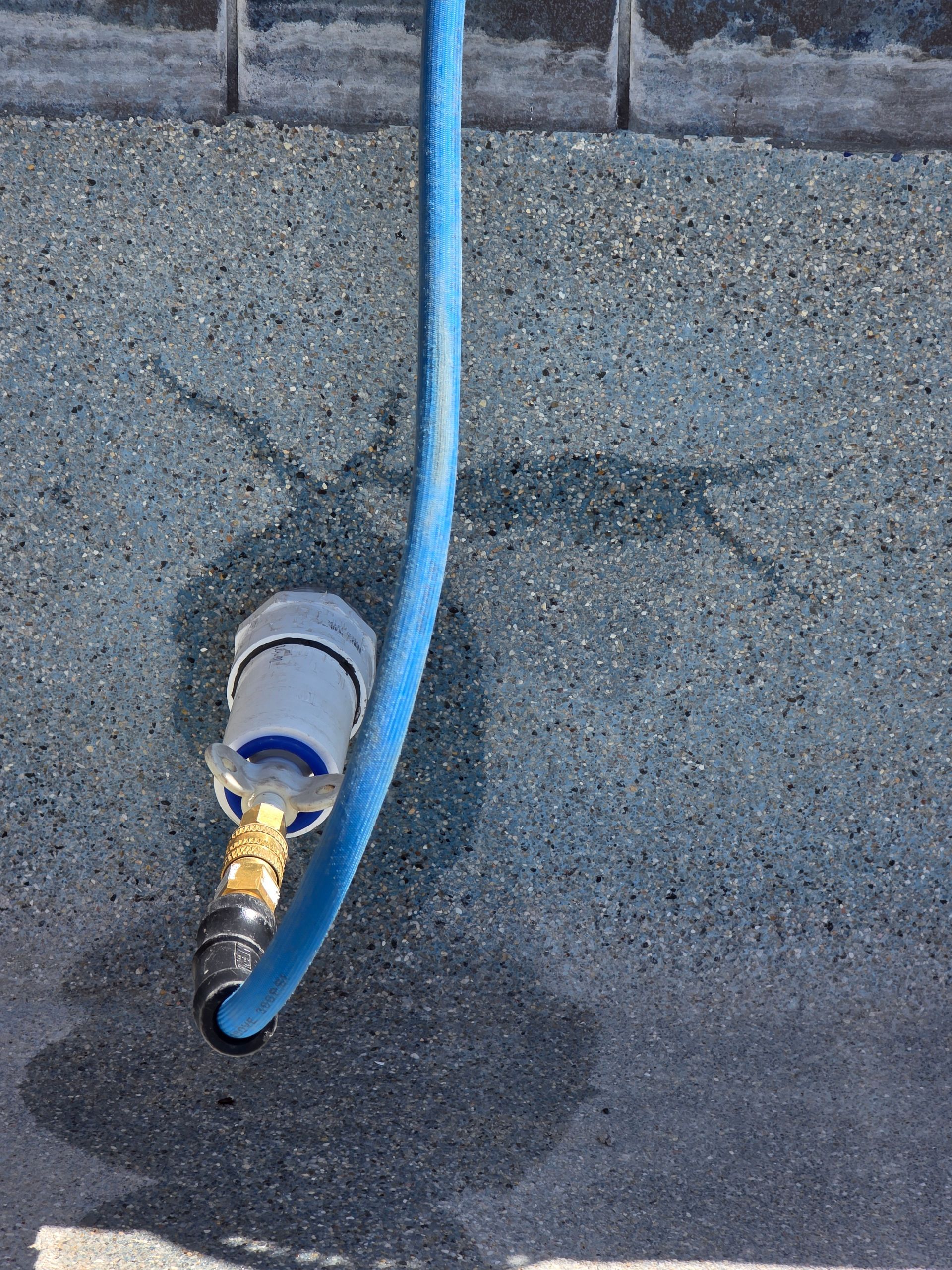 Blue hose connected to a wall outlet on a concrete surface, with a wet dark stain below.