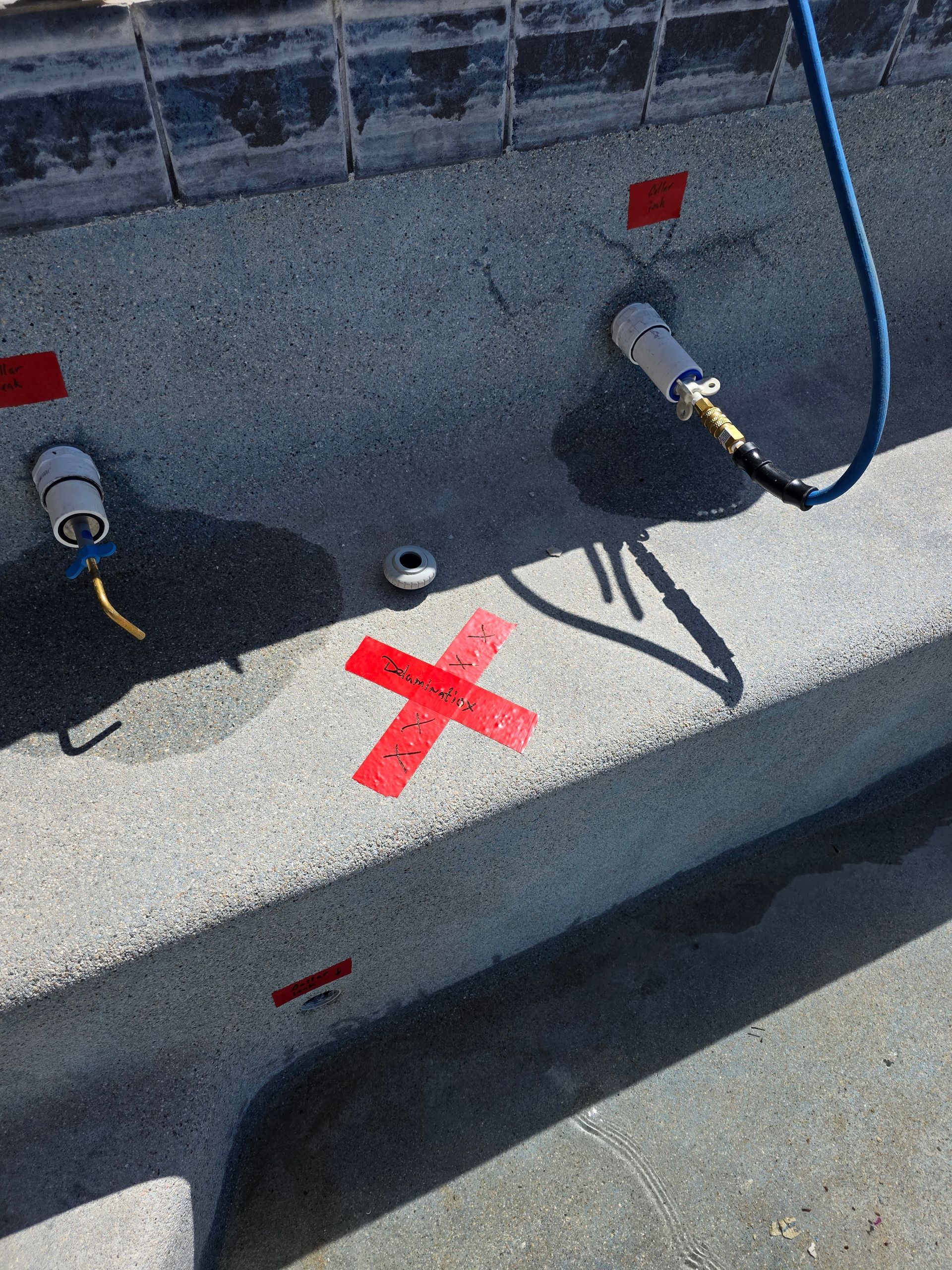 Close-up of gray equipment with red tape marking an X and two connected hoses on a concrete surface