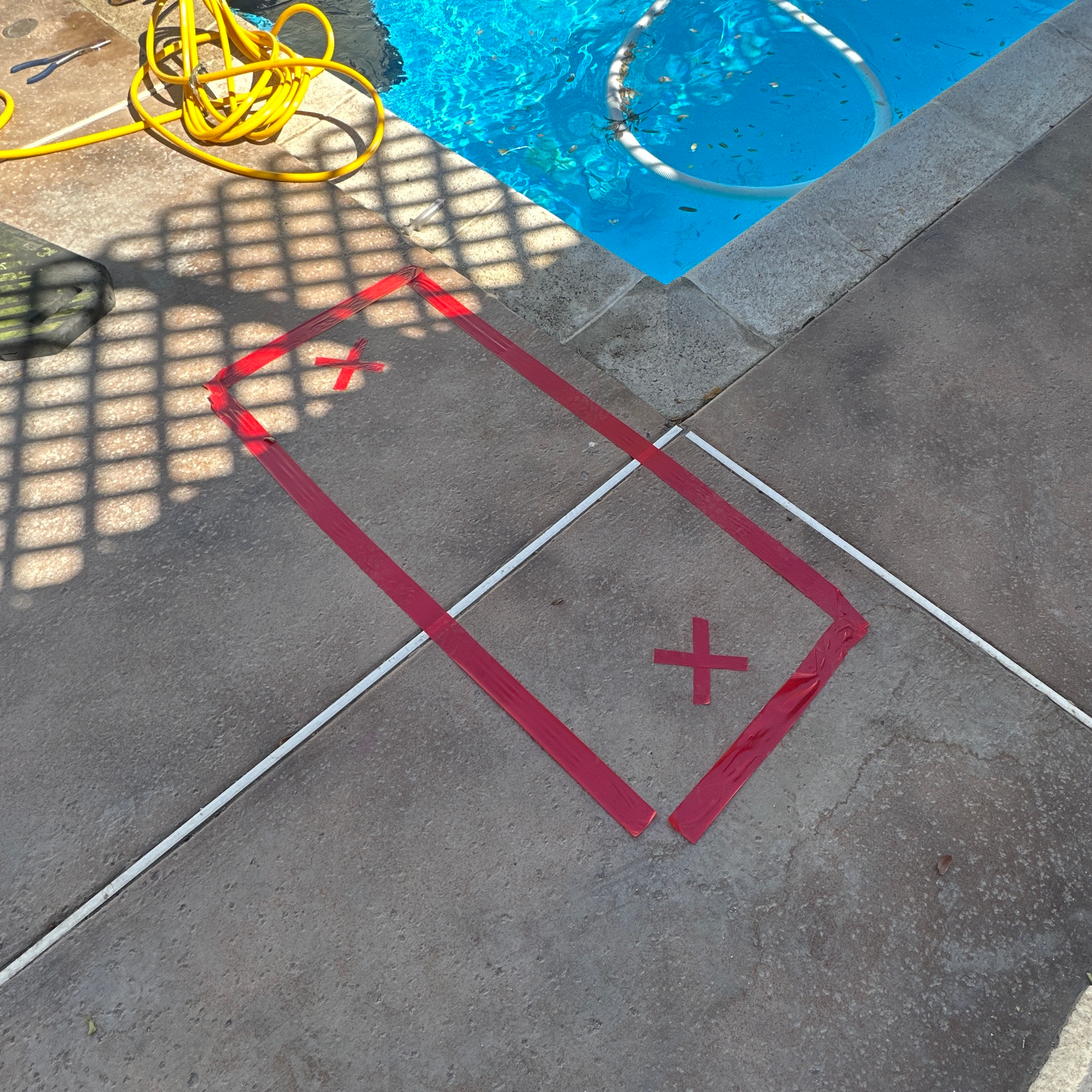 Red tape rectangle marking on a pool deck beside the blue water and hose