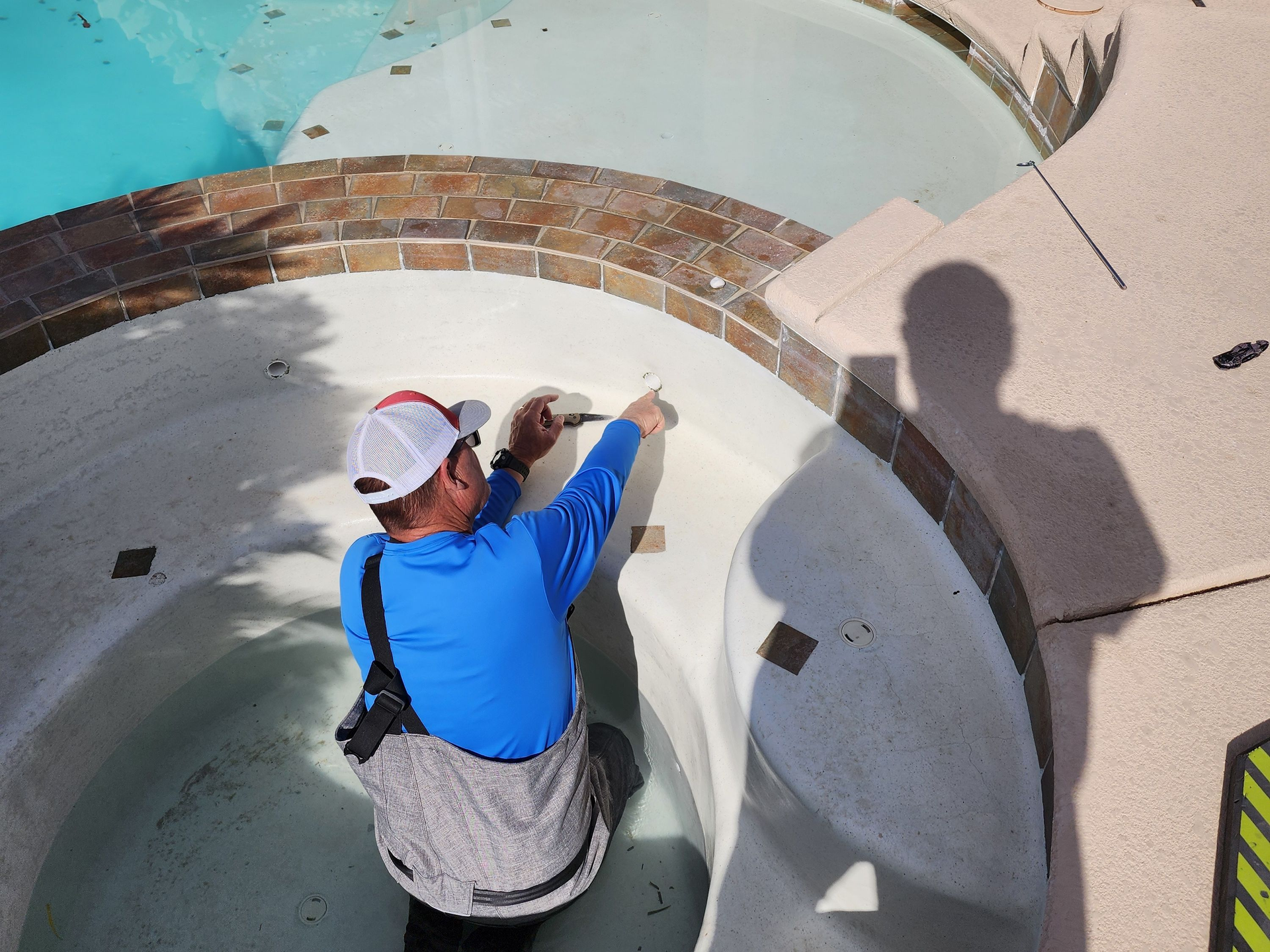 Person in blue shirt and white cap pointing into an empty circular pool or fountain.