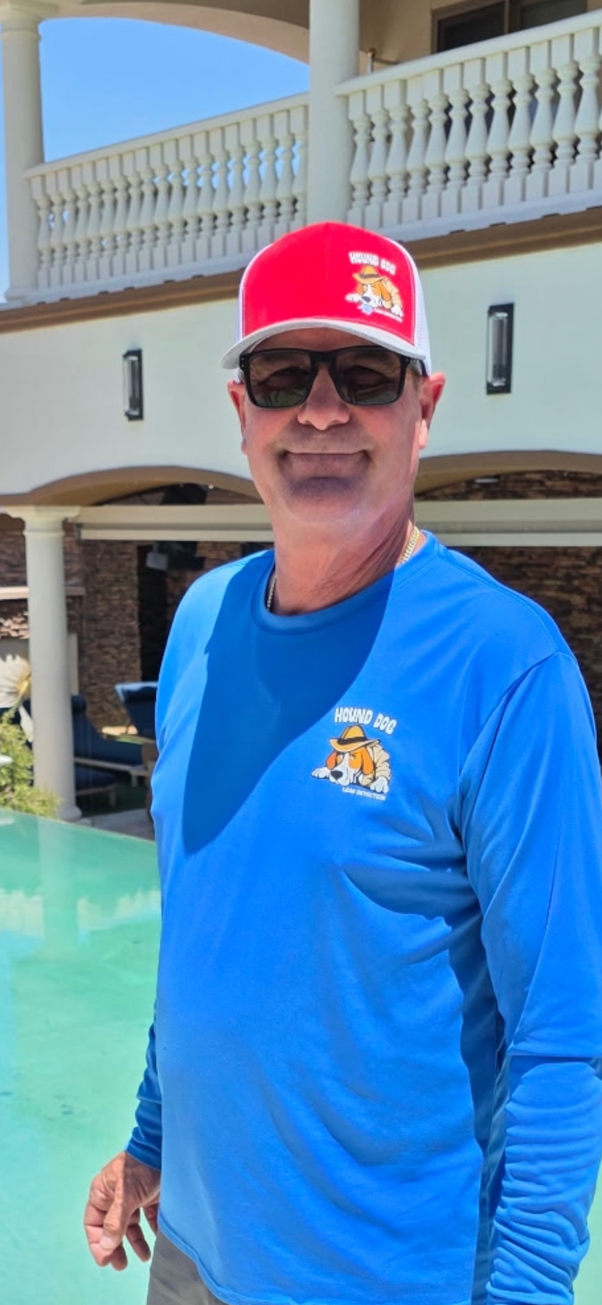 Man kneeling by a pool, holding a yellow rope and giving a thumbs-up near a yellow cord in the water