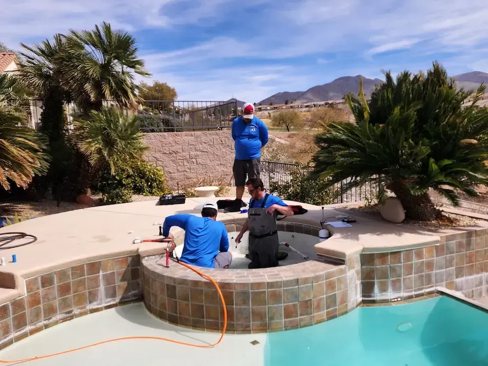 People in a backyard hot tub being cleaned near a pool, with desert landscaping and mountains in the background