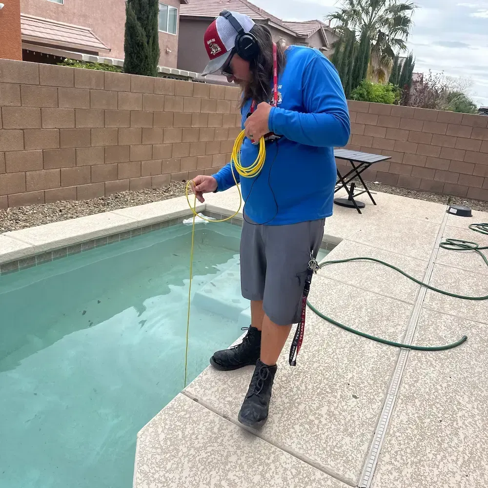 Person in blue shirt measuring pool water with a test strip beside an outdoor swimming pool.