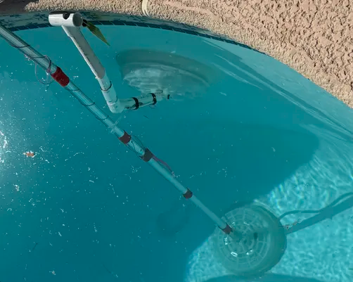 Pool vacuum hose and float line in turquoise swimming pool water near the edge
