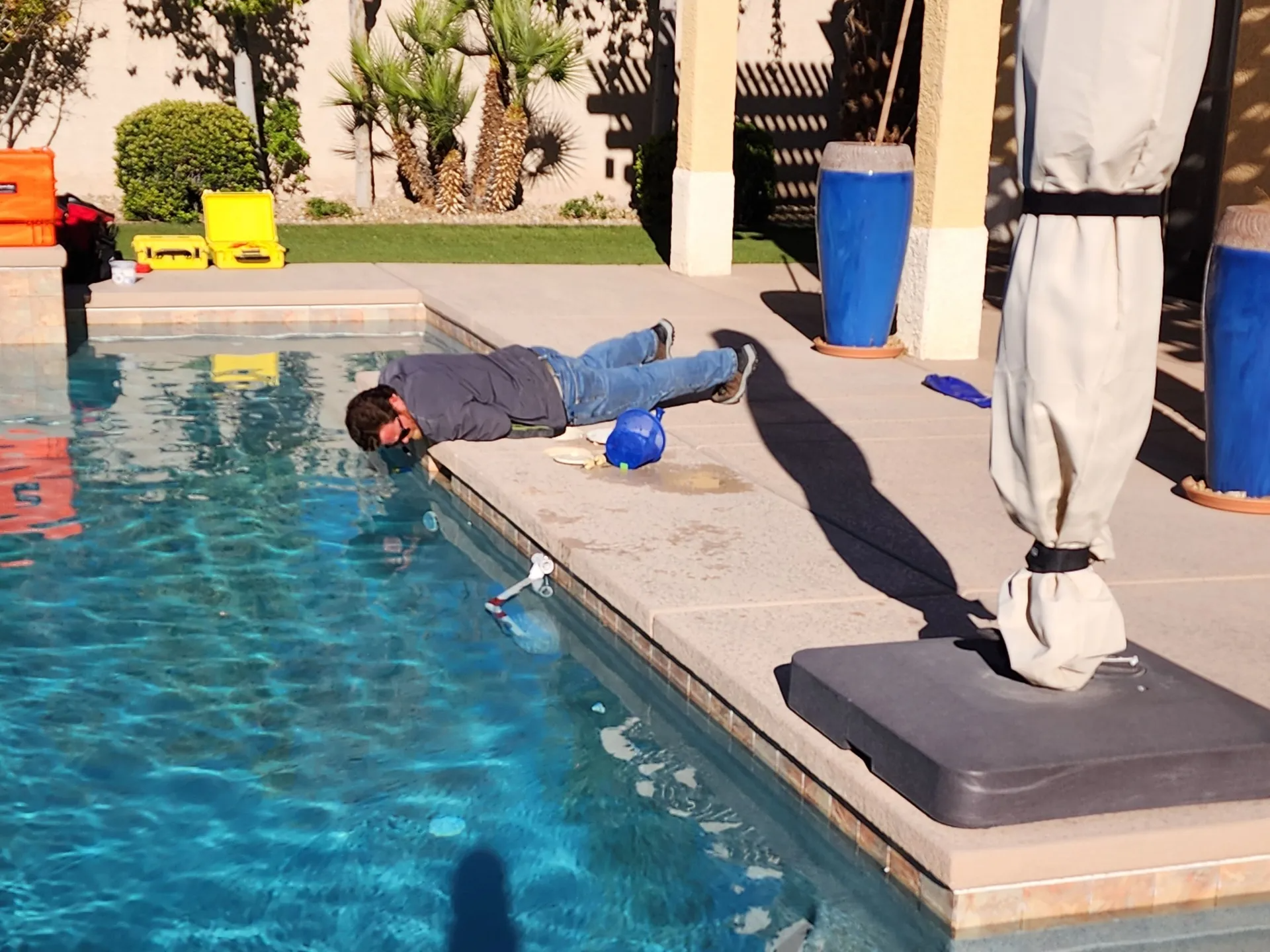 Person lounging on a pool deck beside the water, near a blue towel and lounge chairs.