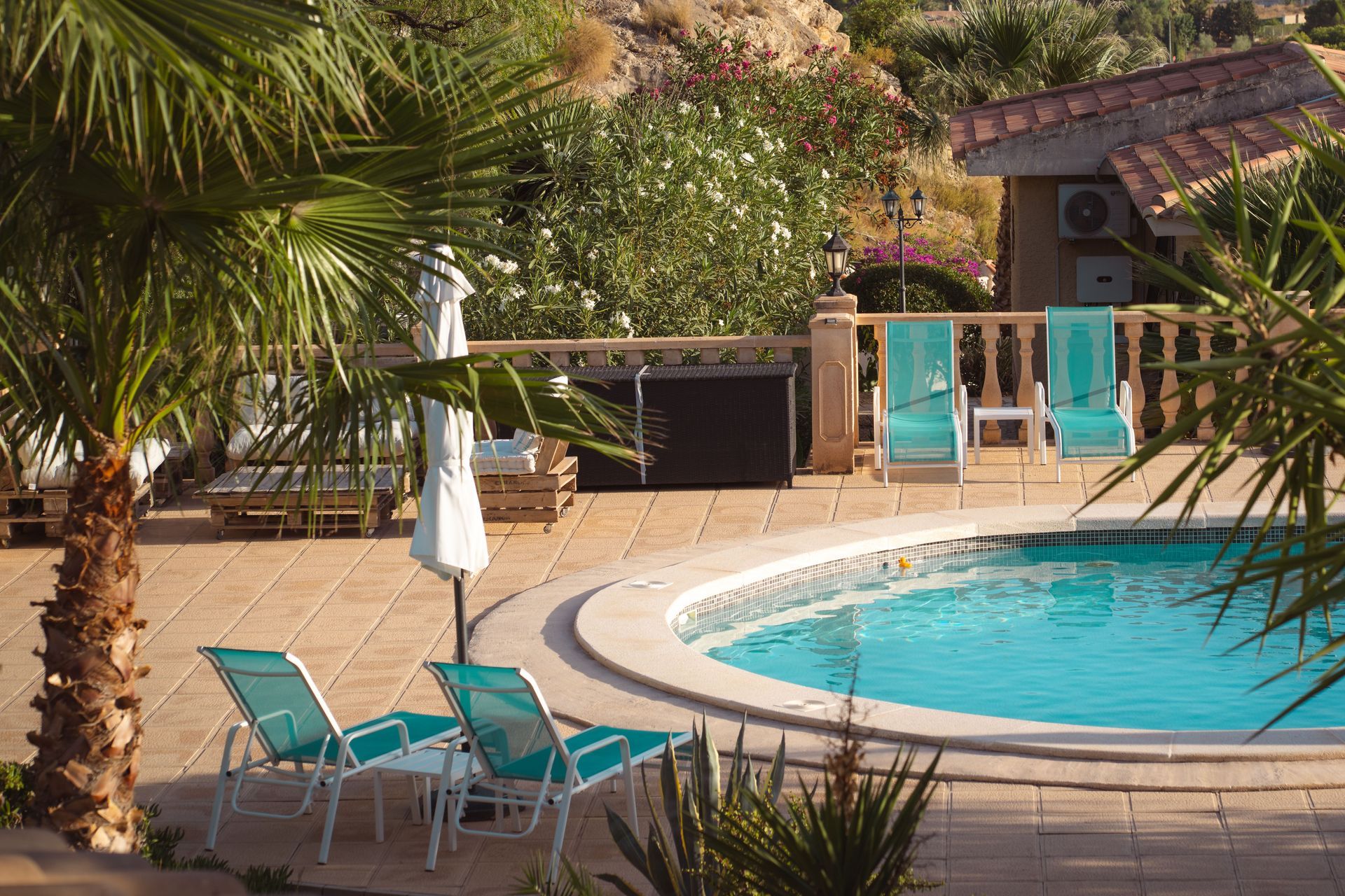 Resort pool with turquoise water, palm trees, lounge chairs, and hillside villas in the background