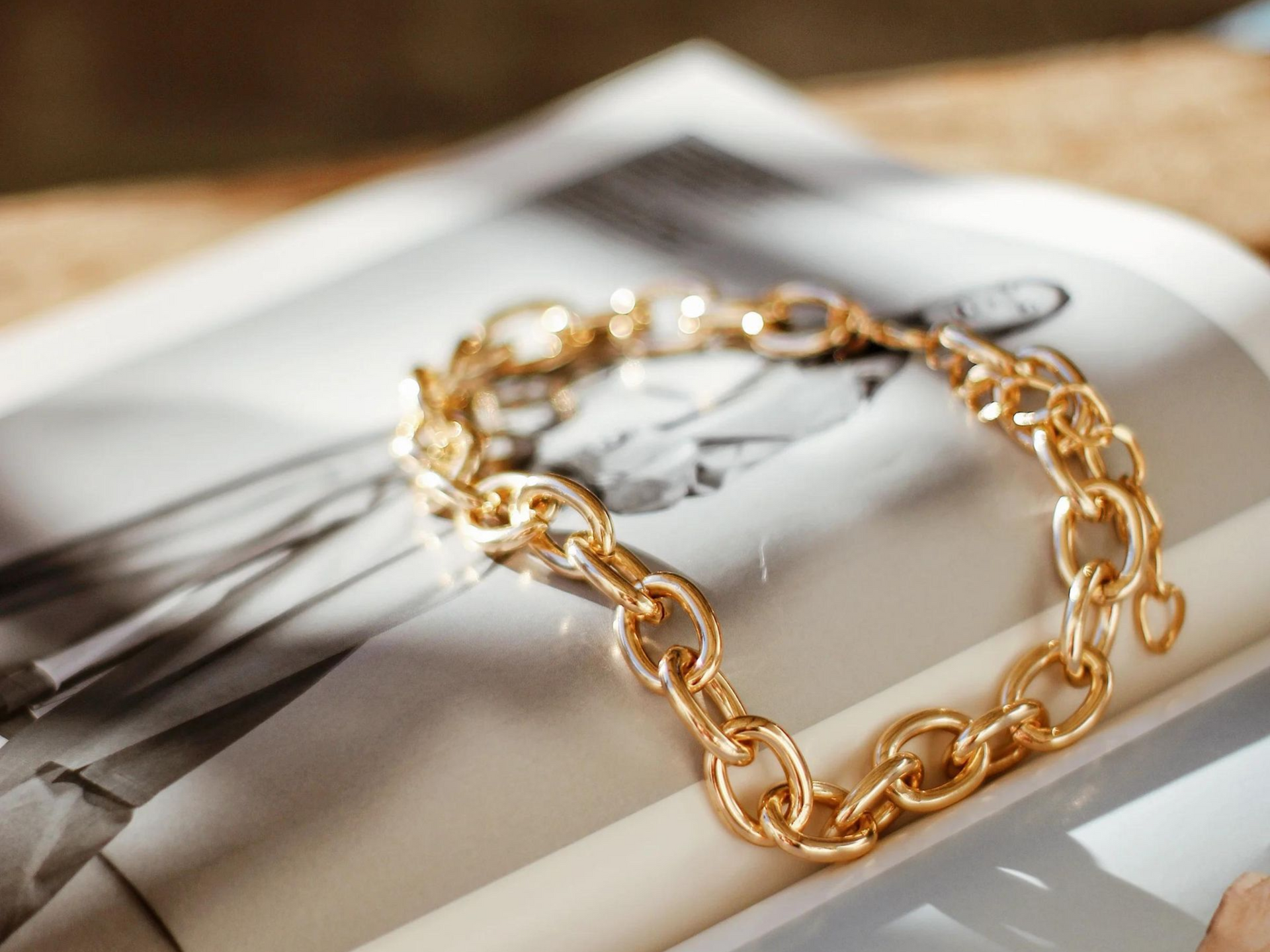 Gold chain bracelet on a magazine page beside a fork and knife on a table