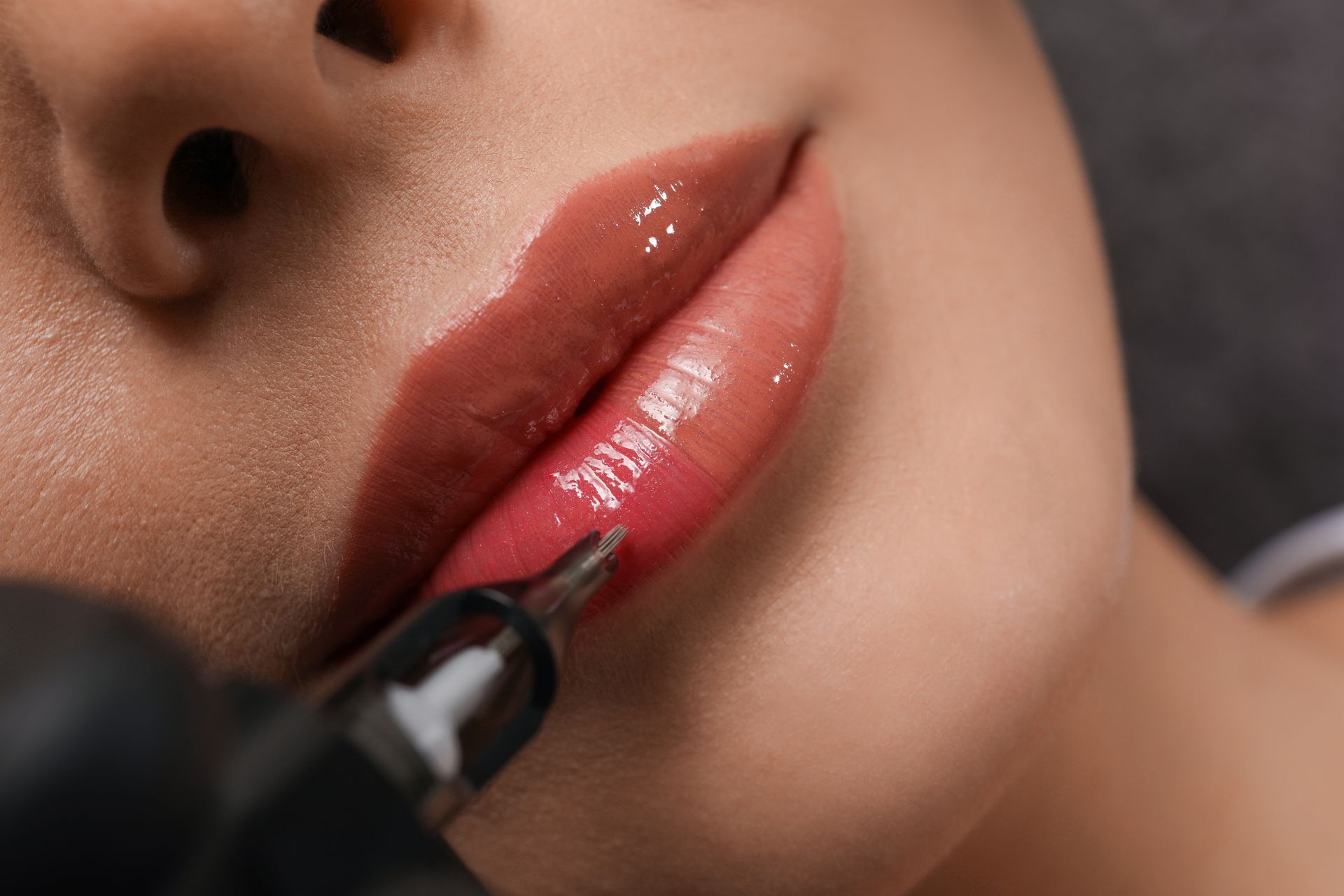 Close-up of lips being lined with a black makeup applicator, glossy pink lipstick visible