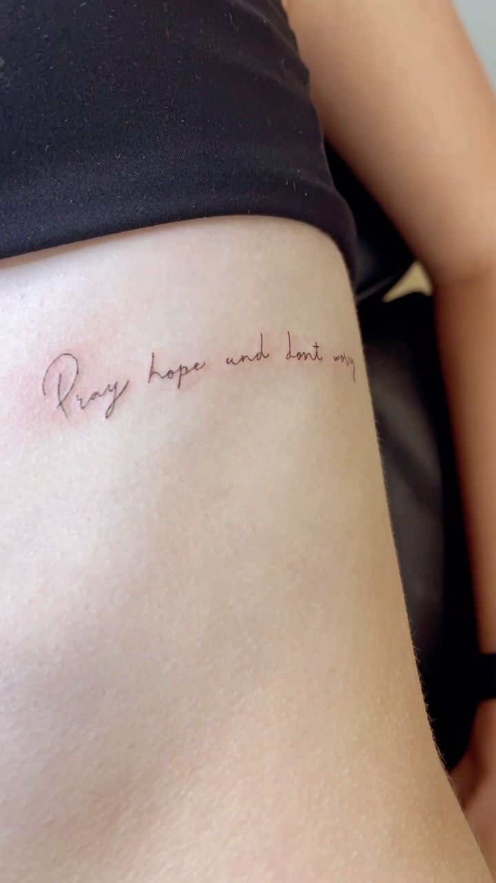 Close-up of a thigh with a small cursive script tattoo on light skin.