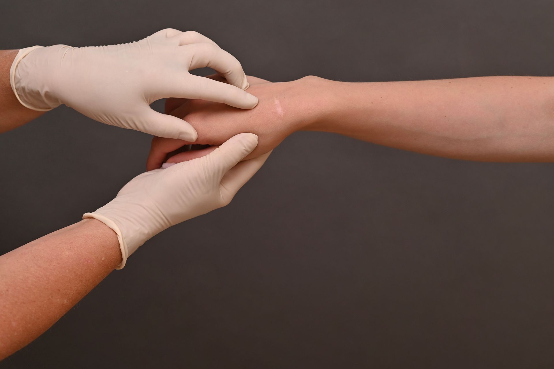 Gloved hands adjusting a wrist on a bare forearm against a dark background