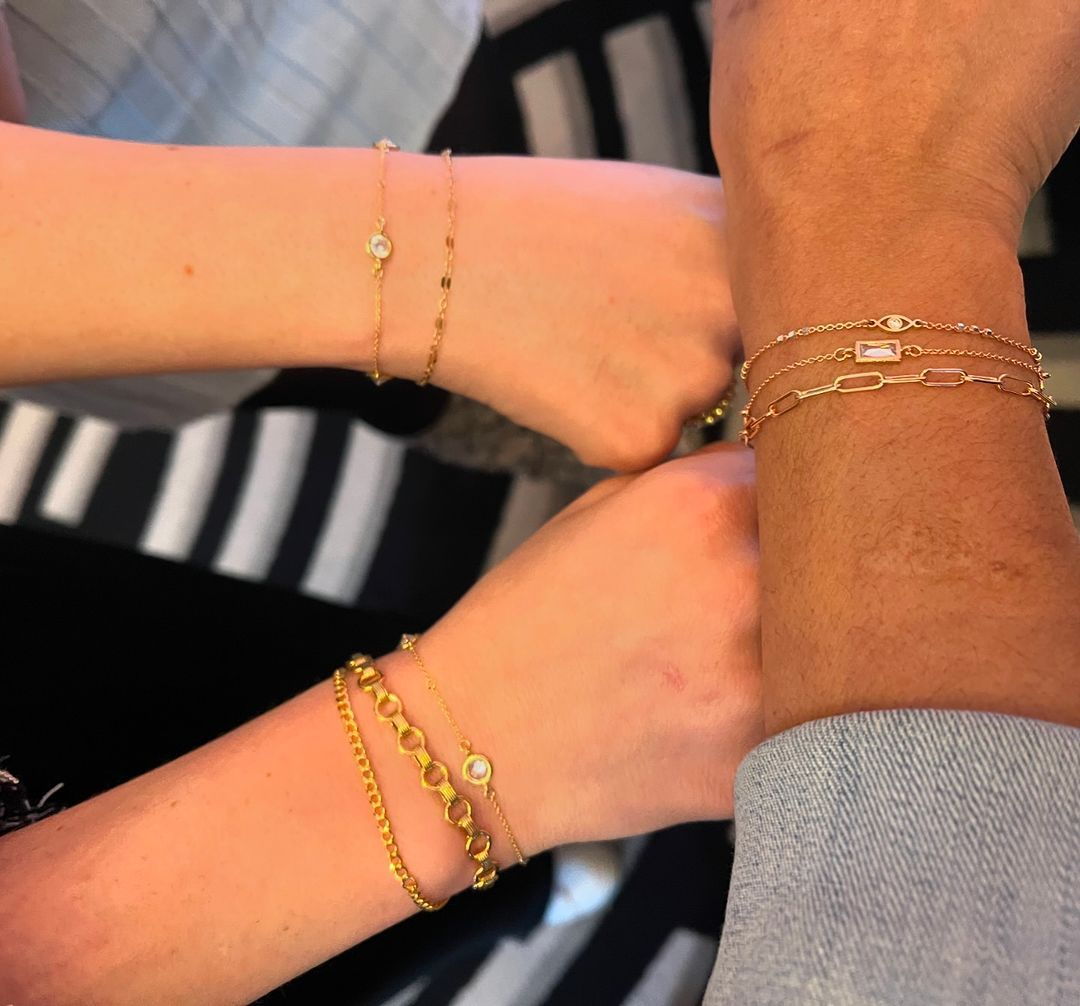 Three wrists with layered gold bracelets joined together in a group gesture