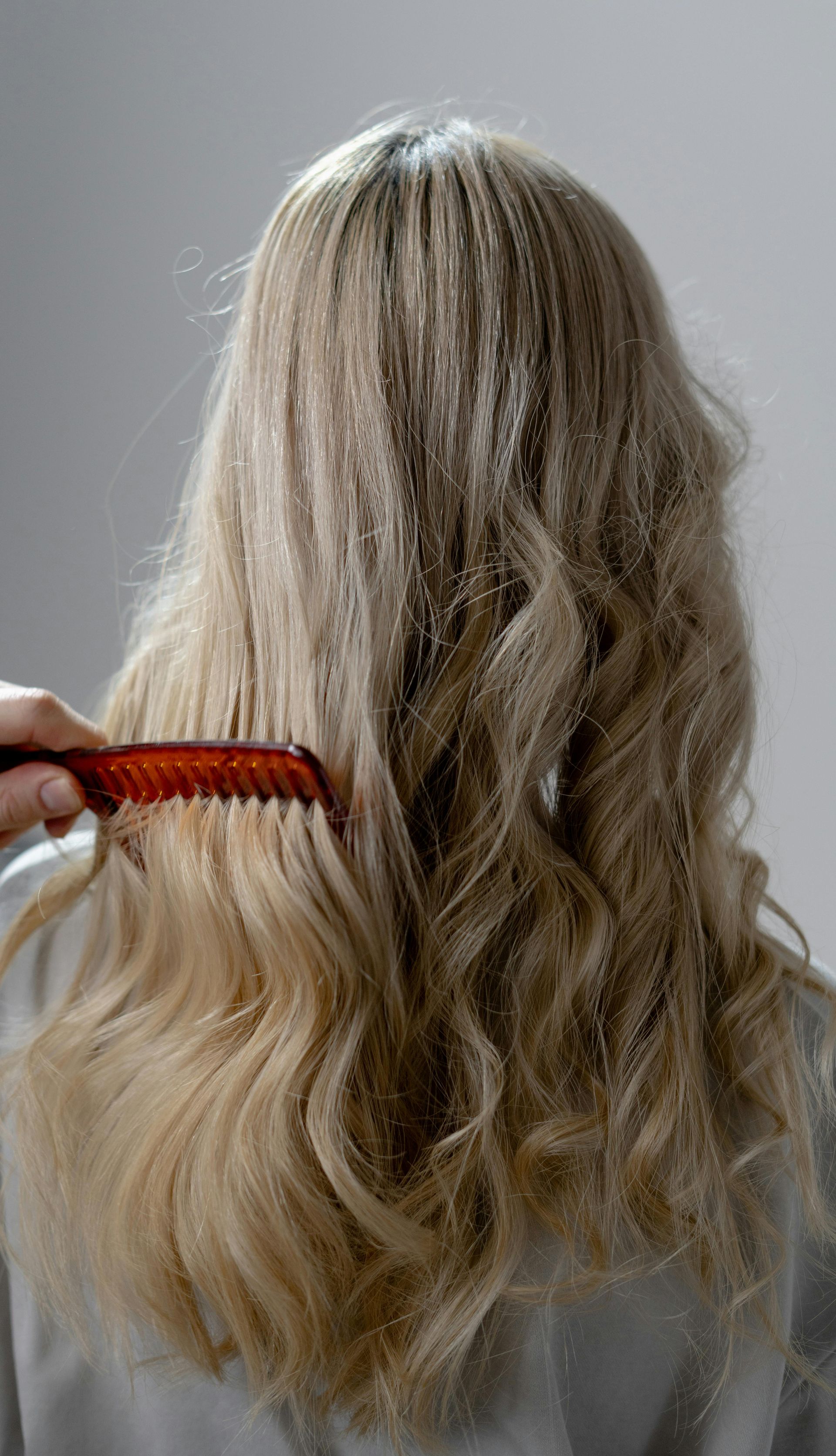 Une femme brosse ses cheveux blonds avec un peigne rouge.