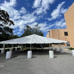 White tent set up in a parking lot outside a beige building under a blue sky with puffy clouds.