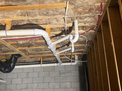 White plumbing pipes snaking across a basement ceiling, connected to a drain and vent.