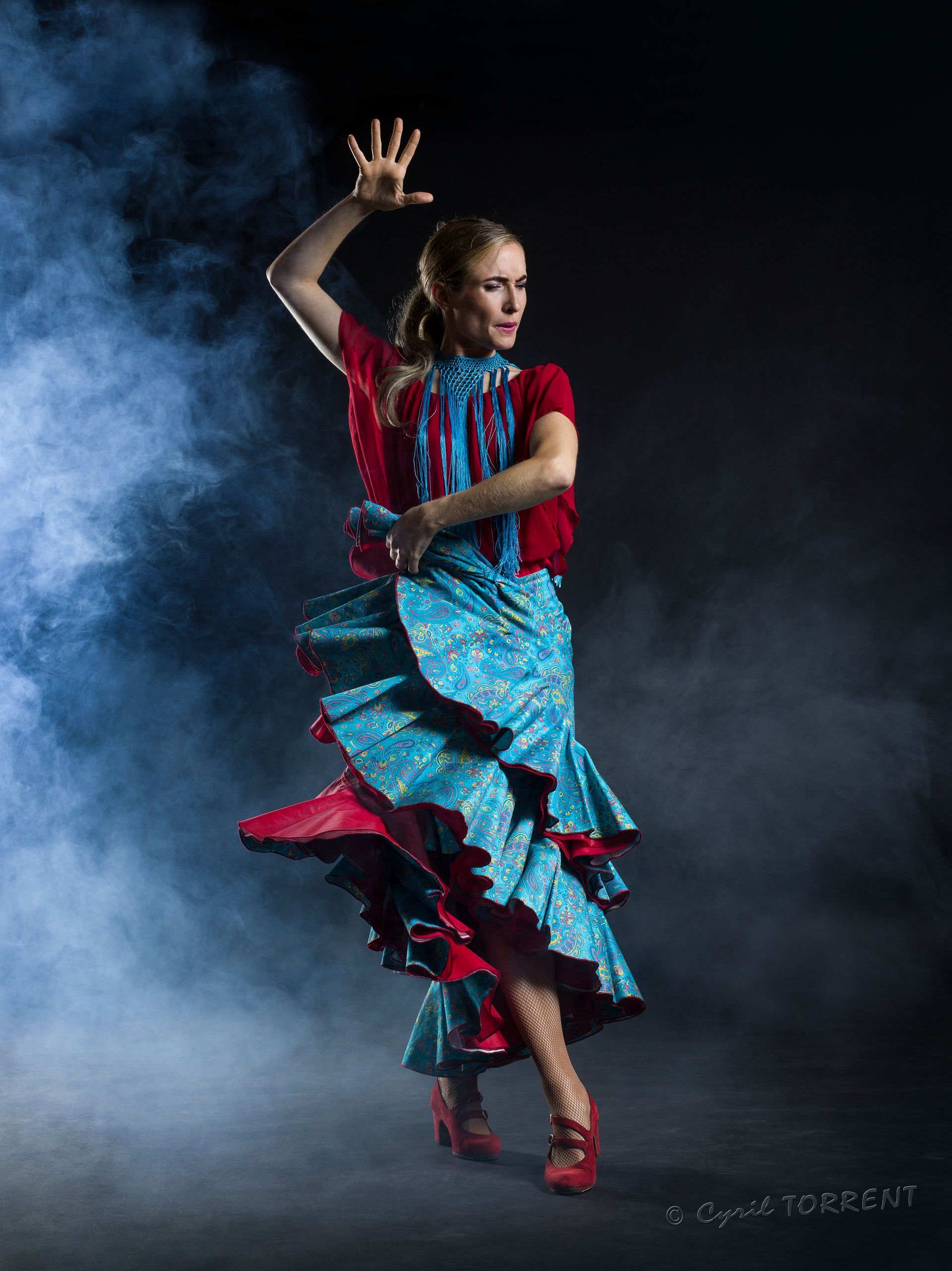Danseuse de flamenco en robe bleue et rouge posant sur un fond sombre et enfumé