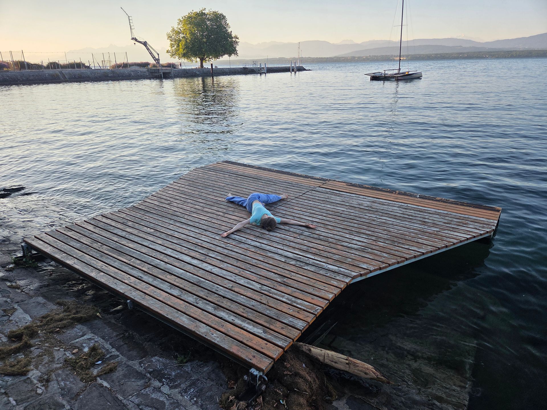 Ponton en bois flottant sur une eau calme, avec un coussin bleu en forme d'étoile de mer au coucher du soleil