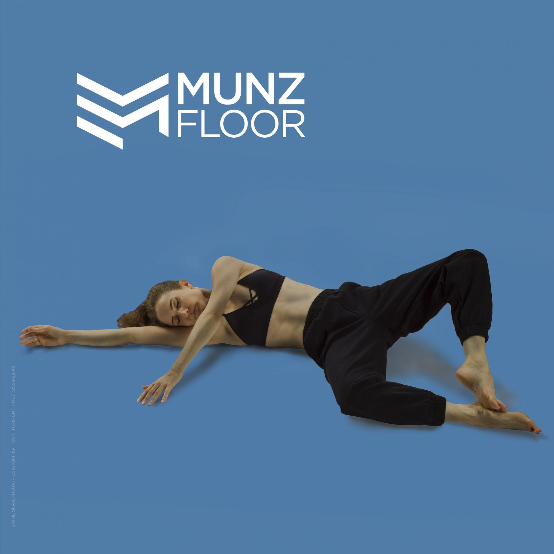 Femme s'étirant sur un sol bleu avec le logo Munz Floor dans un coin.