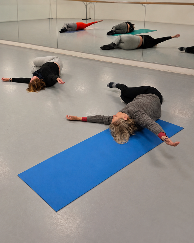 Des personnes allongées face contre terre sur des tapis de yoga dans un studio, les bras tendus pendant un exercice au sol.