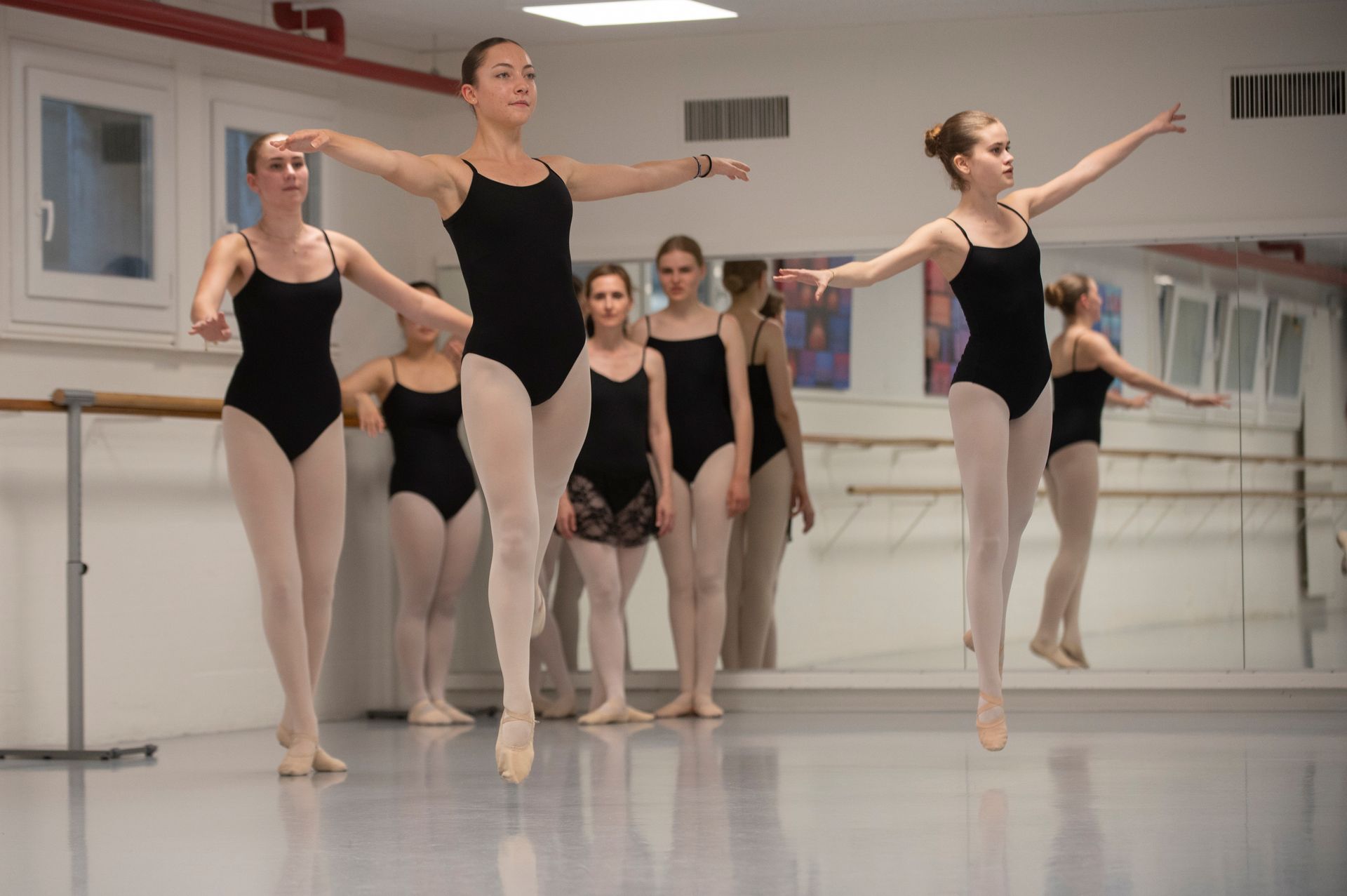 Des danseuses de ballet s'entraînant à la barre dans un studio, les bras tendus et les jambes levées