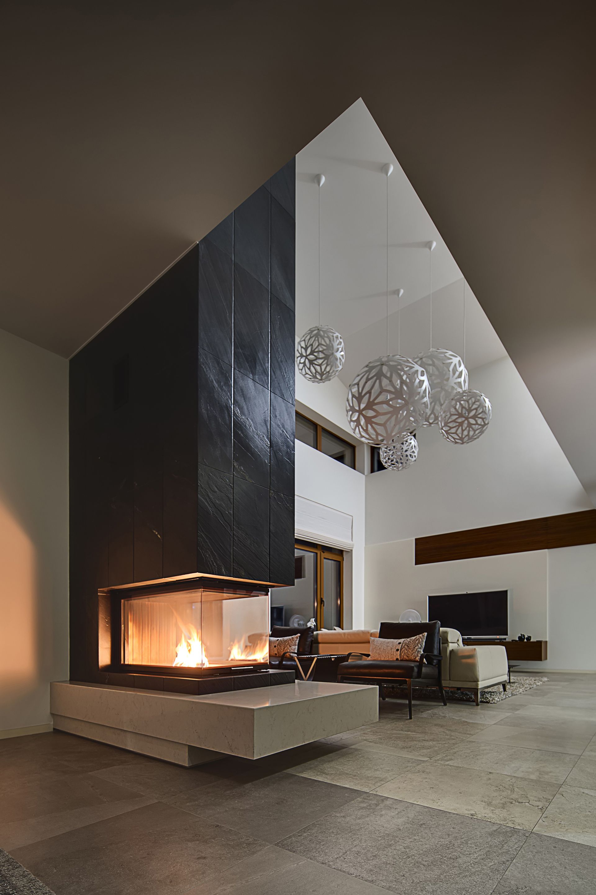 Salon moderne avec cheminée, mur en pierre sombre, plafond blanc et suspensions lumineuses.