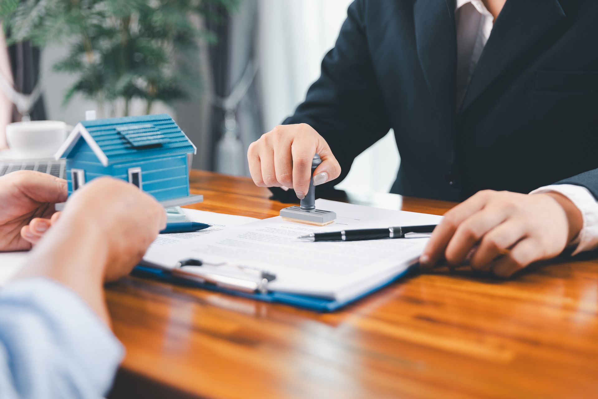 Une personne appose un tampon sur un document, probablement un contrat immobilier, à l'aide d'une maison miniature posée sur la table.