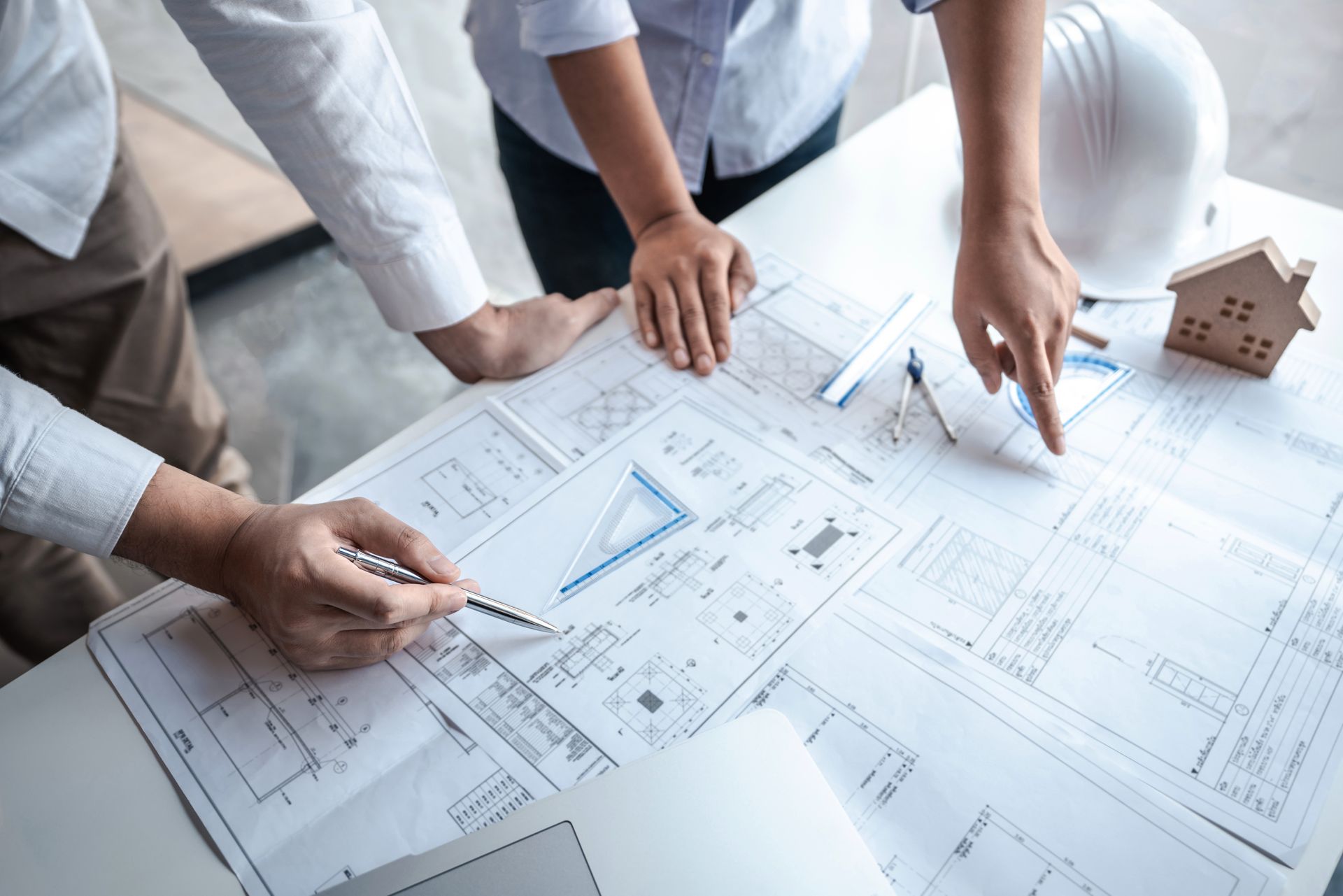 Des mains examinent des plans architecturaux sur une table avec une maquette de maison.