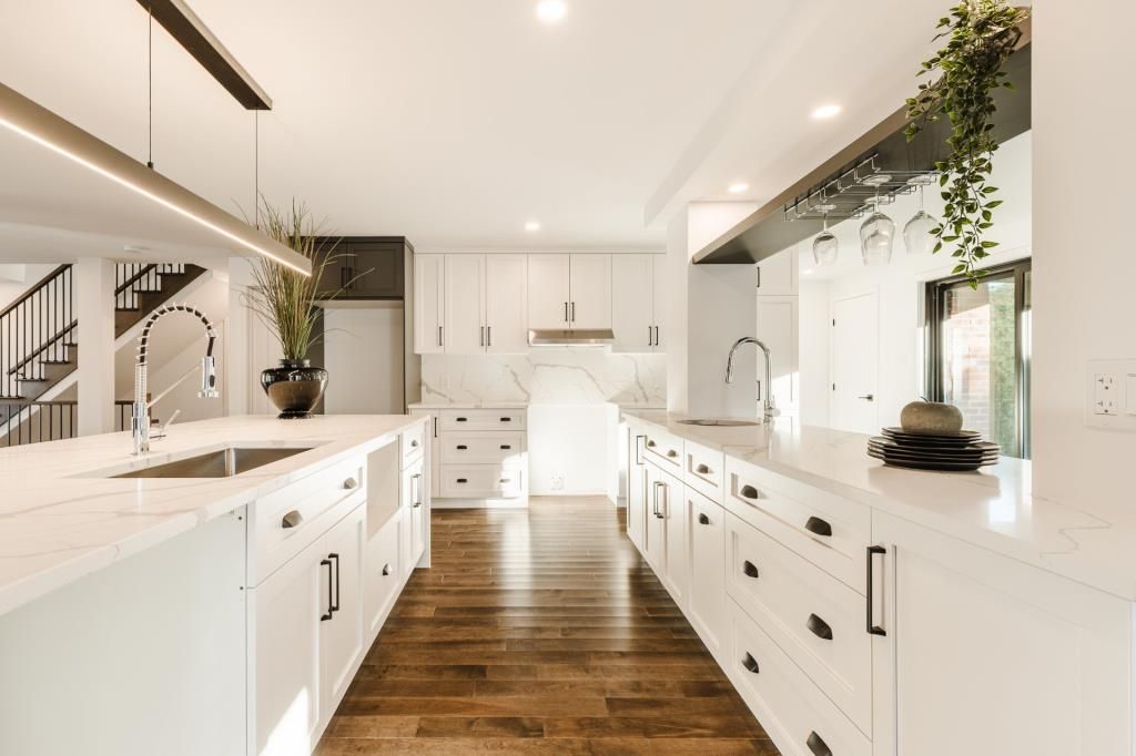 Cuisine lumineuse et moderne avec armoires et comptoirs blancs, planchers en bois et un long îlot.