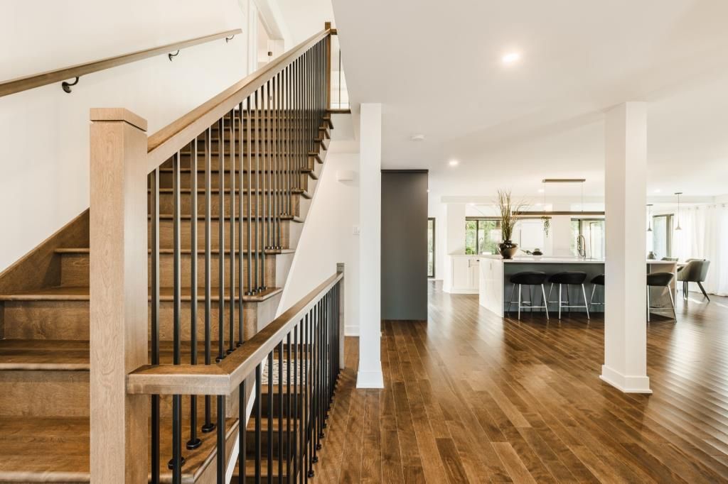 Un escalier en bois avec des rampes noires mène à un espace de vie lumineux et ouvert avec parquet.