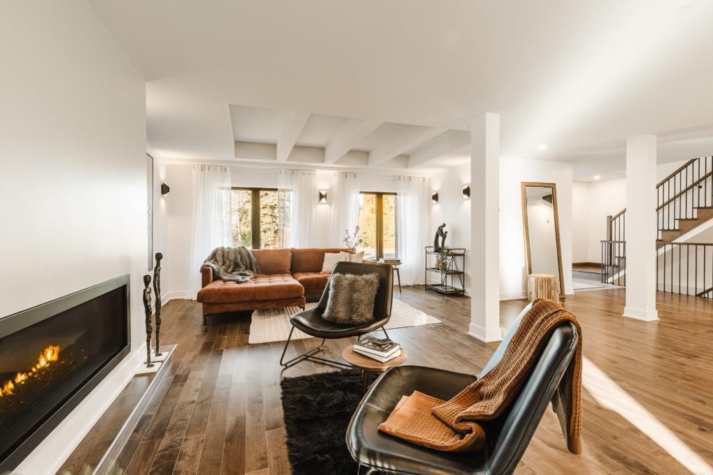 Vaste salon avec cheminée, fauteuils en cuir et canapé marron. La lumière du soleil inonde la pièce.