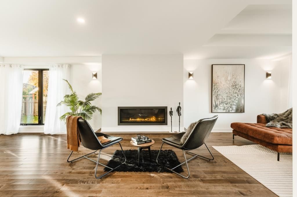 Salon moderne avec cheminée, deux fauteuils noirs, canapé en cuir marron et parquet.
