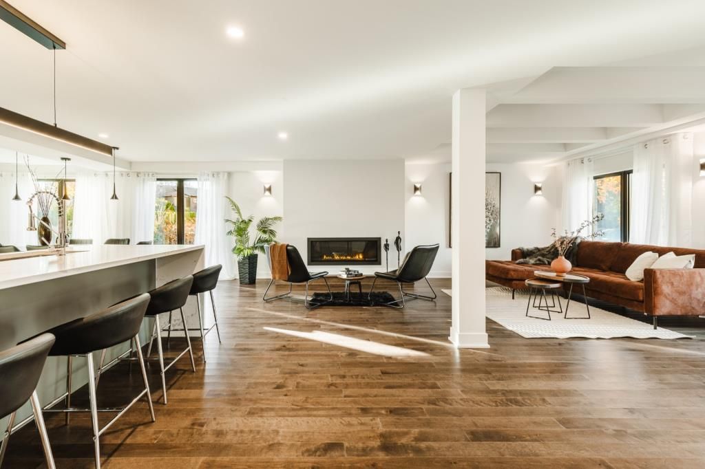 Espace de vie moderne à aire ouverte avec bar, coin salon, cheminée et parquet.