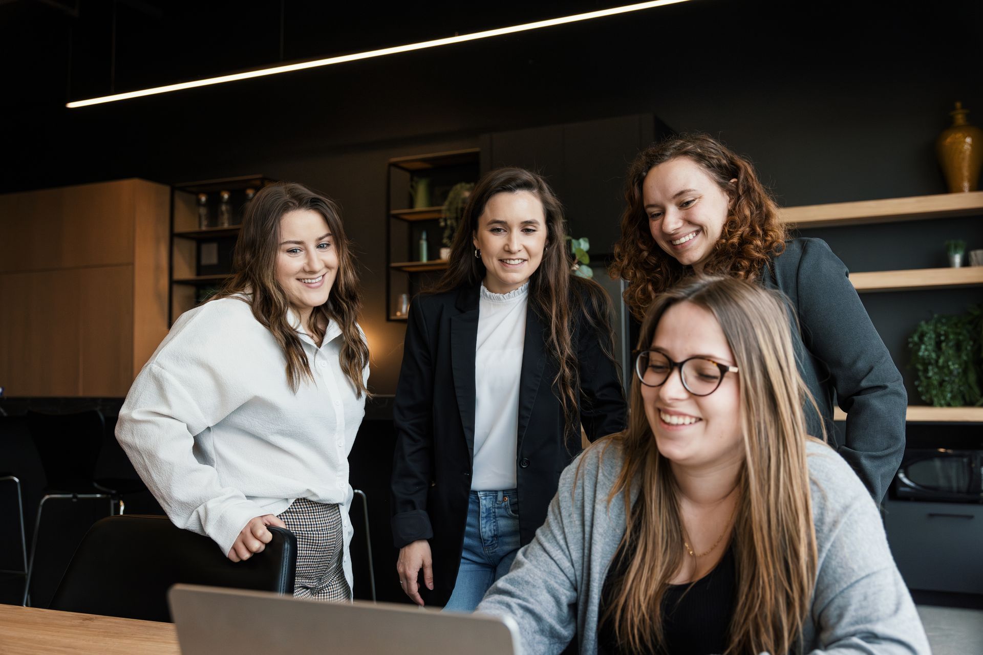 Quatre femmes souriantes, réunies autour d'un ordinateur portable dans un bureau moderne.
