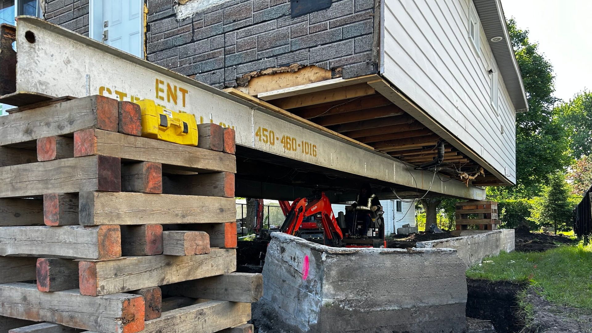 Maison en construction sur blocs de béton empilés, avec poutres apparentes et outils en dessous.