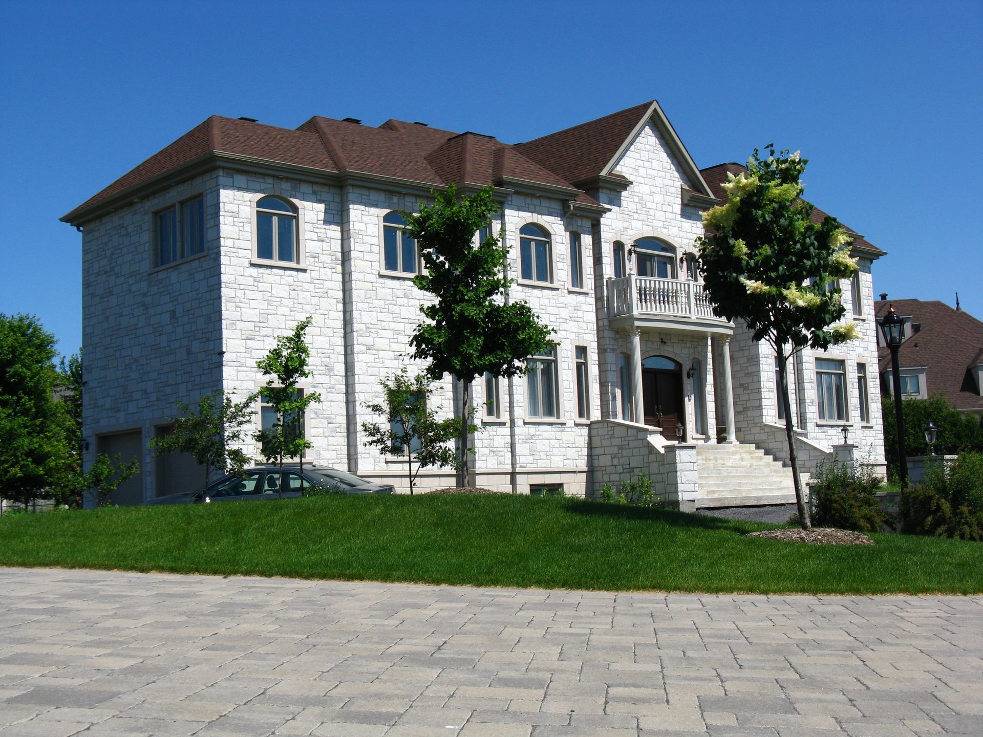 Maison de deux étages en briques blanches avec toit brun et pelouse verdoyante par une journée ensoleillée.