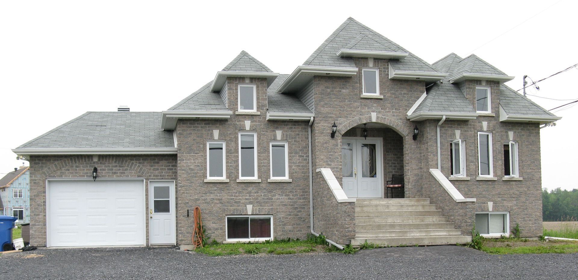 Maison en briques grises avec un toit gris et une porte de garage blanche.
