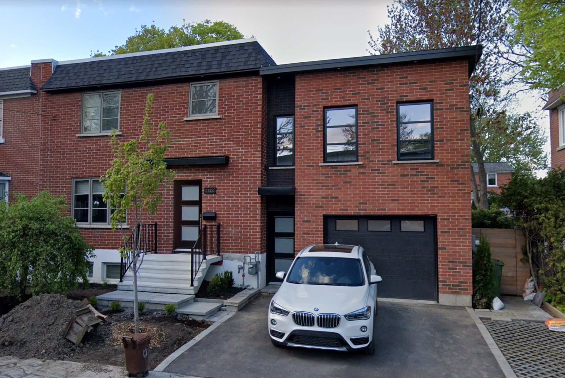 Maison en briques avec boiseries noires et garage ; voiture blanche dans l'allée.