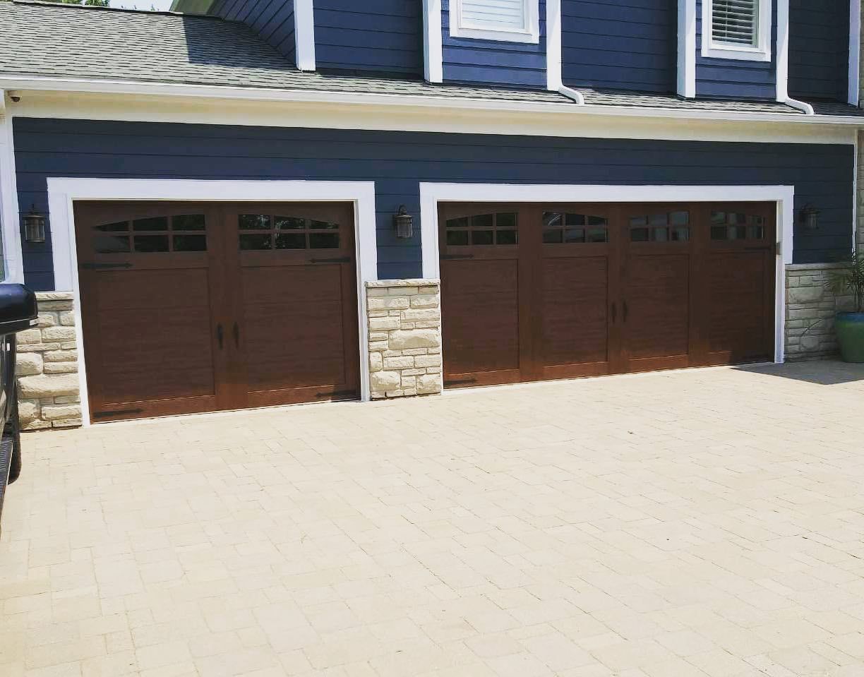 Two-car garage with brown doors and stone accents, set against a blue-sided house with a light-colored driveway.