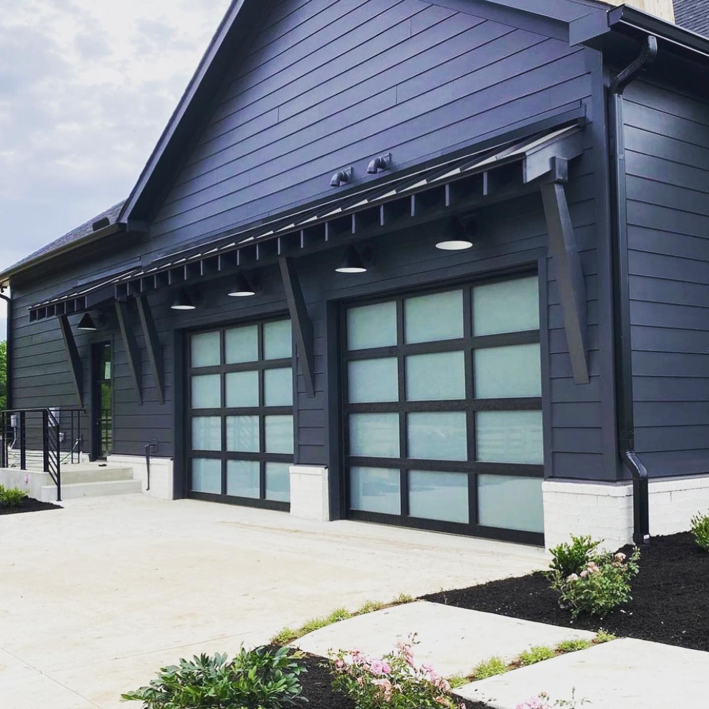 Dark blue modern garage with glass doors and a concrete driveway.