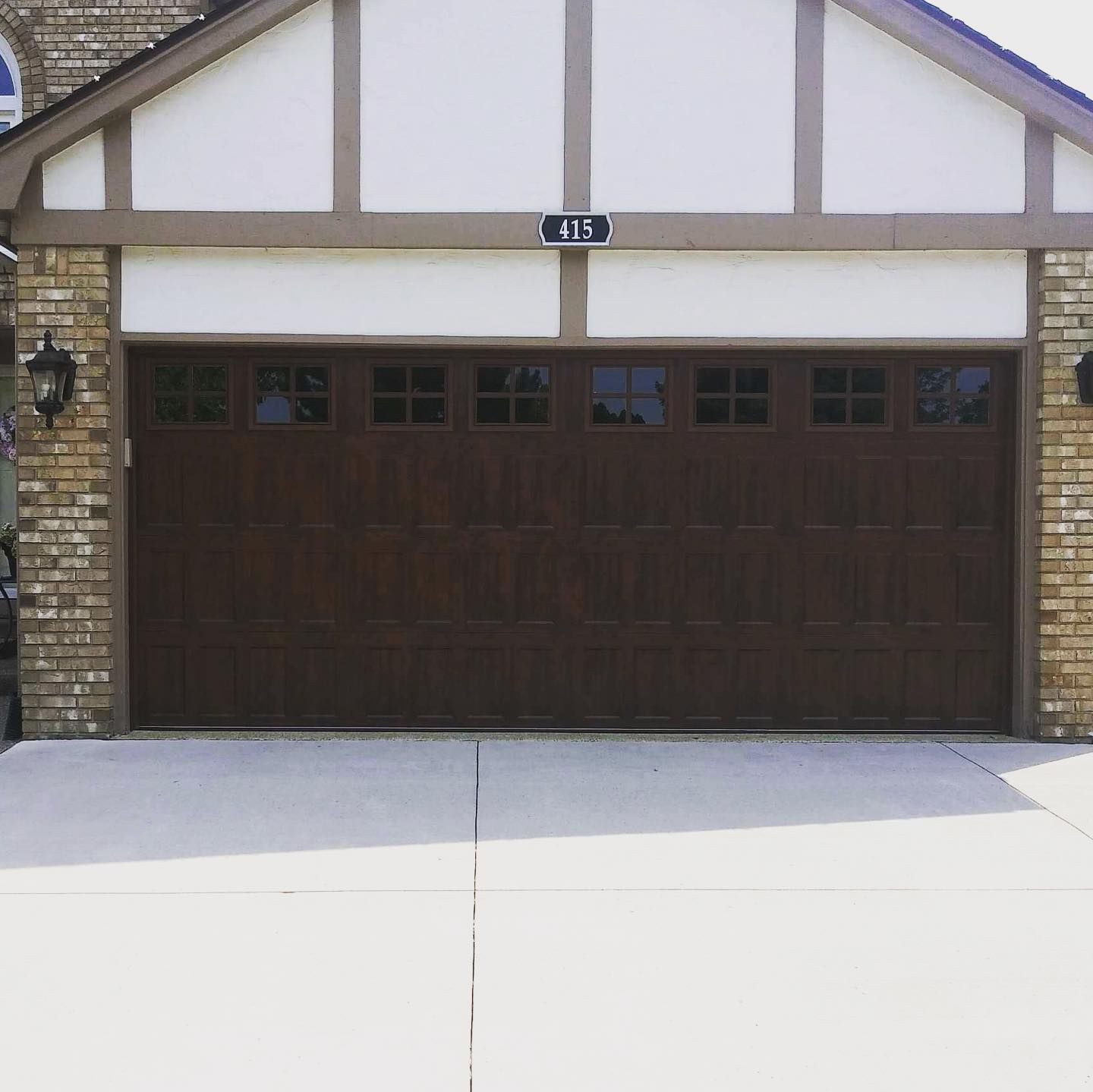 Brown garage door with windows, brick accents, and beige trim. House number 