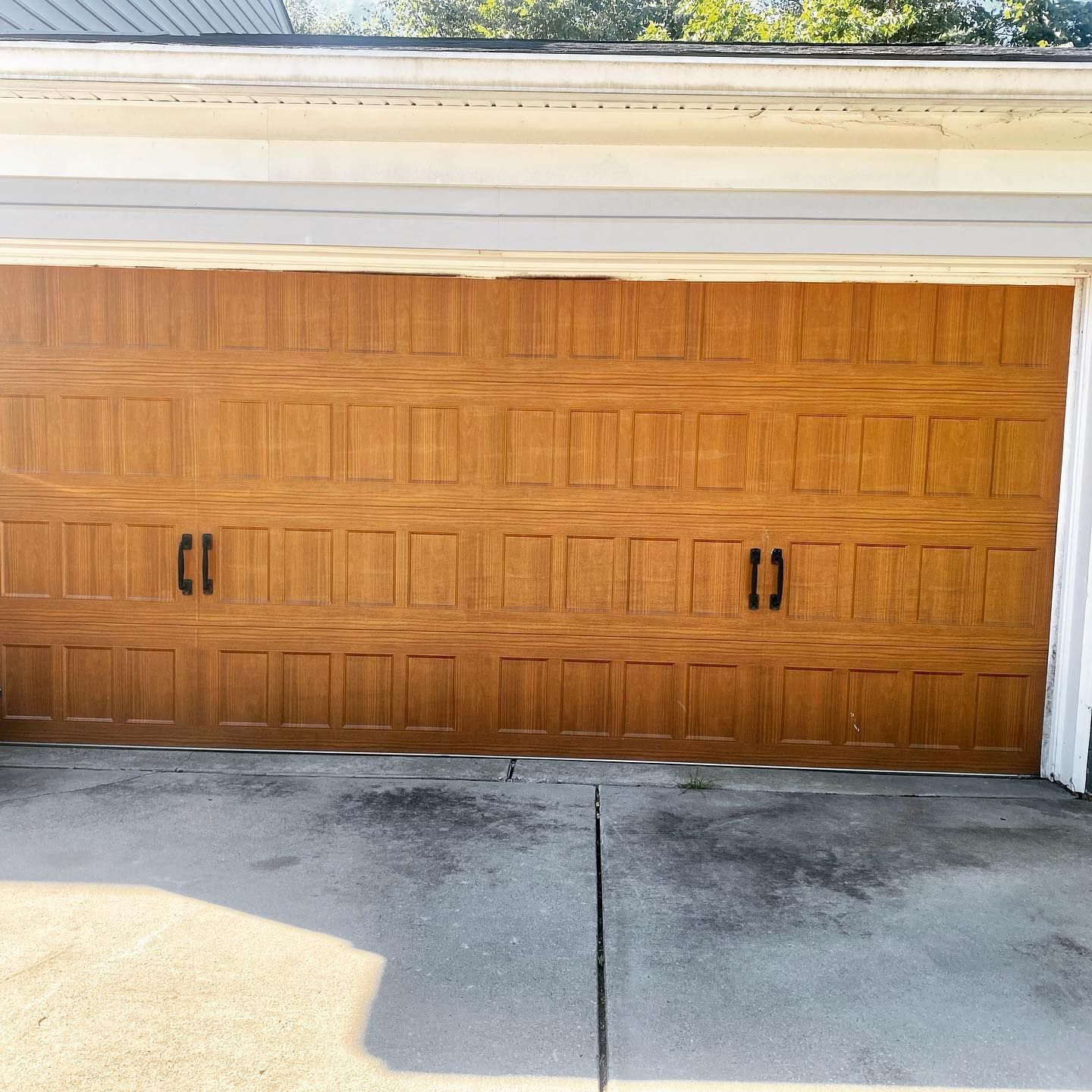 Brown garage door, closed, with two black handles. Concrete driveway in front.