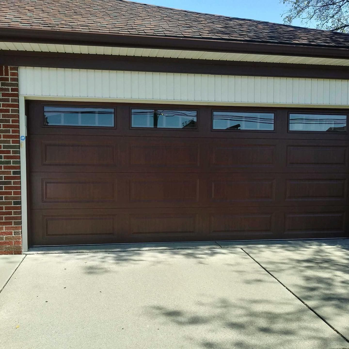 Brown garage door with windows, on a brick building with a concrete driveway.
