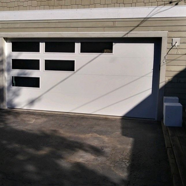 White garage door with six black-paned windows, gray trim, and concrete driveway.